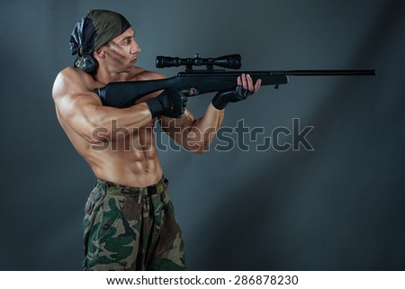 Man to aim in aim. He wants to shoot a sniper rifle. He had big muscles and naked torso.