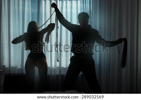 Only visible silhouettes of men and women. Man beaten with a whip bound woman in a dark room near the window.