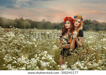 Two girls standing in an embrace in the field. At the head of girls wreaths of flowers.