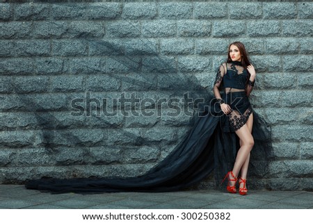 Girl in a long black dress standing near the wall. The dress fluttering in the wind.