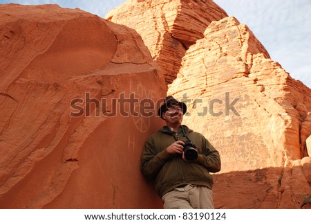 Man leaning against a red rock with peace sign as graffiti engraved on the rock.