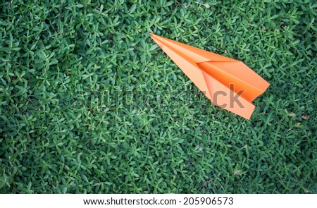 orange paper plane on green leaves