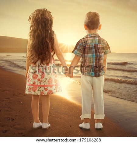 Back view of little girl and boy holding hands at sunset. Love, friendship concept
