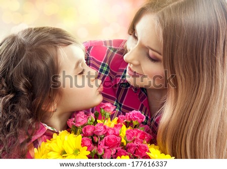 Daughter kissing happy mother with flowers. Mother`s day concept. Family holiday