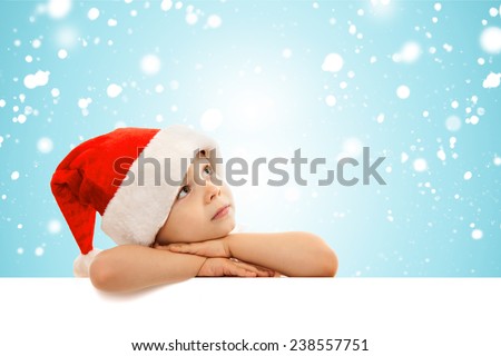 Happy little boy in Santa hat peeking from behind blank sign billboard. Space for Your Text. Sale, holidays, christmas, new year, x-mas concept.