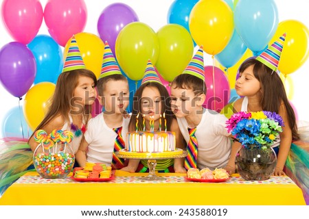 Group of joyful little kids celebrating birthday party and blowing candles on cake. Holidays concept.
