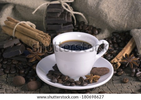 Cup of coffee with coffee beans, chocolate and spices on a wooden surface
