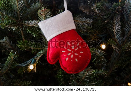 A felt red and white mitten ornament hangs in a gently lit Christmas tree