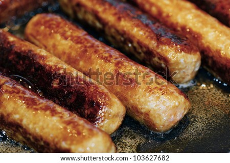 Delicious pork and beef sausages being cooked in a frying pan with oil and fat making bubbles, perfect for nutrition, cholesterol or healthcare topics.