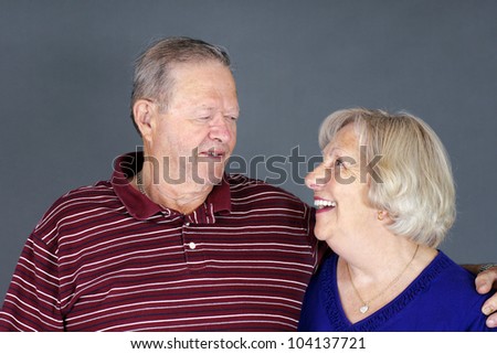 Happy and healthy senior couple laughing together, studio shot over grey background.