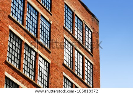 Old red brick building or factory with many small windows with top corner close to tumbling down because of cracks.