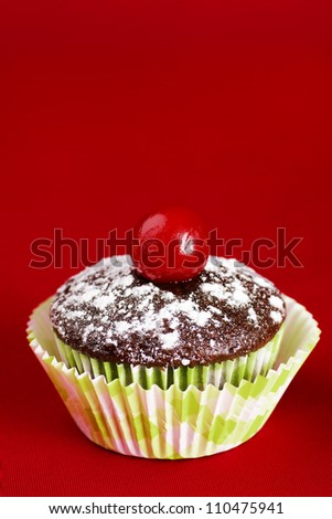 Delicious chocolate cupcake topped with powdered sugar and maraschino cherry over red background for copy space.