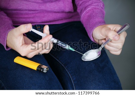 Drug paraphernalia: young woman junkie preparing heroin or the likes for injection with the syringe.