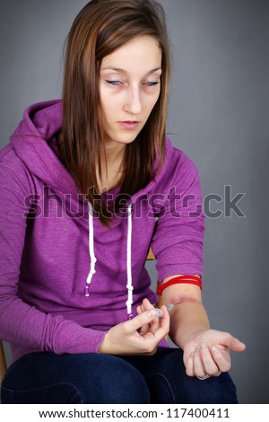 Young woman junkie, getting high injecting drugs, like heroin, with seringe in her arm; great for substance abuse and narcotics related social issues.