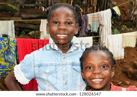 Real candid portraits of black African girls, sisters with big smiles, at home in front of clothesline in their backyard, great for future of developing countries.
