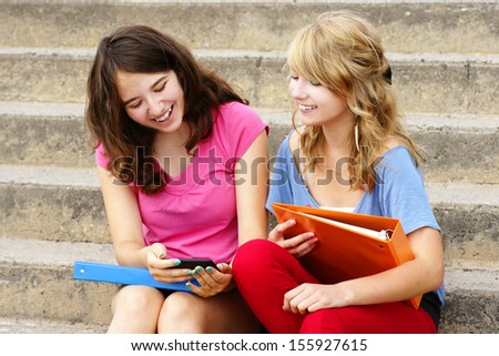 Two teenager girls laughing at texto or internet on their cell phone or mobile