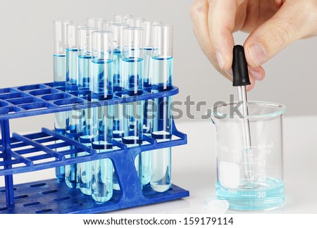 Test tubes with blue liquid, man hand with dropper: chemistry, biology or other science concept