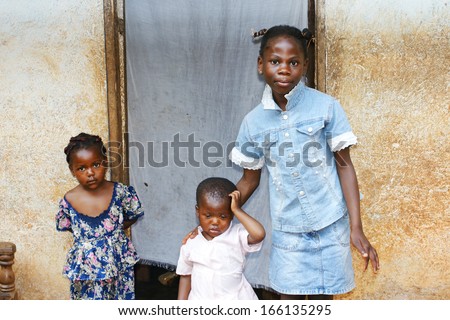 Three black African girls, sisters from a larger family, by their house\'s doorway