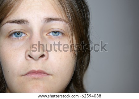 Real natural young woman with stunning eyes but expressing much sorrow, depression and sadness. Three quarter portrait on gray background with copy space.