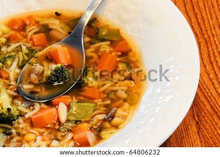White bowl of hearty vegetable homemade soup on wooden kitchen table, good for your health and tummy.