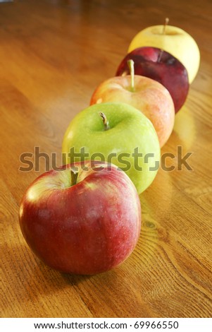 Apples of all kinds in a row on a kitchen wooden table: cortland, granny smith, gala, red and golden delicious.