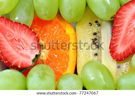 Fun fruit mix background with green grapes, strawberries, kiwi and oranges, focus on the orange and kiwi.