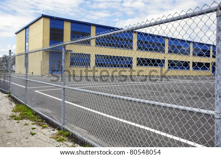 Increasing security of an old small school by restricting access with a gate or wire mesh fence courtyard asphalt playground.