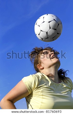 Real female soccer or football player during a match, reaching to hit the ball with her head and score a goal with sky and stadium spot lights in background.