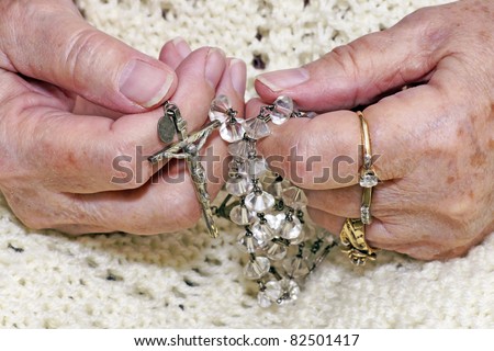 Hands of a senior woman holding a vintage crystal rosary to pray.