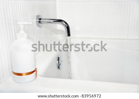 Water running out of old style faucet in the acrylic tub of a crisp white new bathroom with corrugated ceramic tiles and soap dispenser.