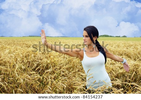High pat on horse single whip tai chi position performed by a young woman connecting with nature while exercising in a wheat field.