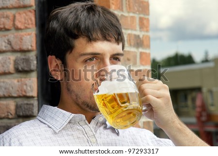 Portrait of a sad young man drinking beer out of glass bok on pub\'s outdoor terrace.