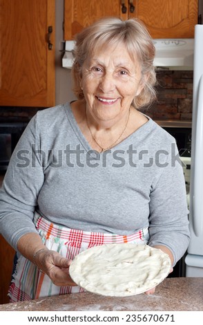 Happy senior woman or grandma showing homemade meat pie in her kitchen