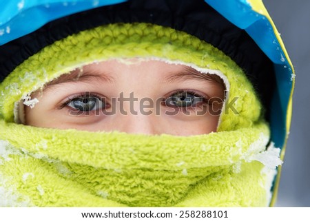 Closeup of bundled up blue eyed little boy with snow flakes details