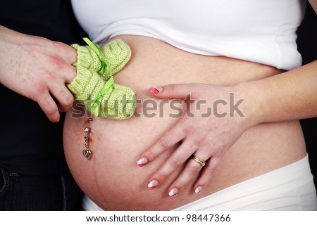 Studio shot of an expecting young married couple with dad to be holding green knit bootees on his wife\'s pregnant belly.