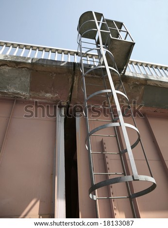 Circular ladder with ring supports leading up to top of Orange Metallic Construction Platform against blue sky