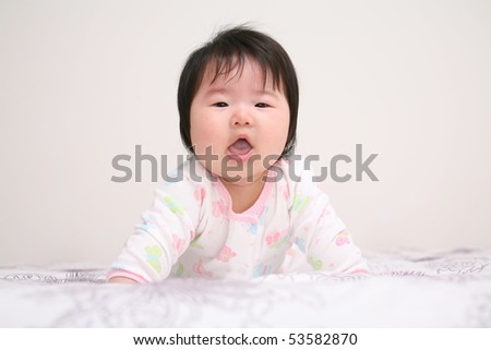 Very Cute Asian Baby with Mouth Open Looking Forward Dressed in White Jumpsuit on Bed