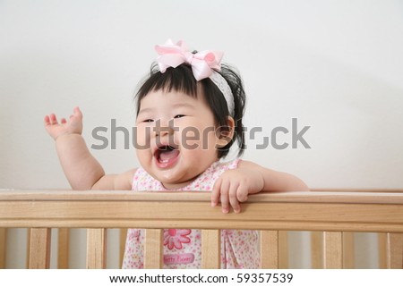 Very Pretty Nine Month Old Baby Asian Infant Girl Saying Hello from Wooden Crib with Pink Bow in Pink Bodysuit