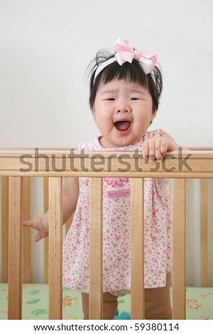 Beautiful Nine Month Old Baby Asian Infant Girl in pink dress with pink ribbon in wooden crib screaming
