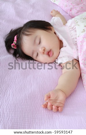 Sleeping beautiful nine month old asian baby infant girl with pink bow in hair on bed sheet