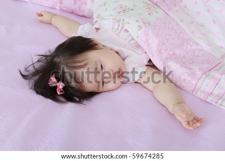 Beautiful Nine Month Old Asian Baby Infant Girl with pink bow in hair under blanket just waking up