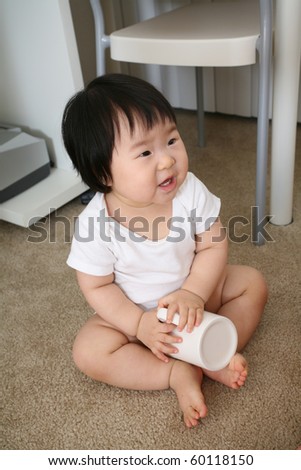 Beautiful and lovely ten month old asian baby infant girl in white shirt sitting on carpet playing with mug