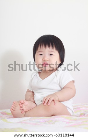 Beautiful and lovely ten month old asian baby infant girl in white shirt sitting on bed docilely