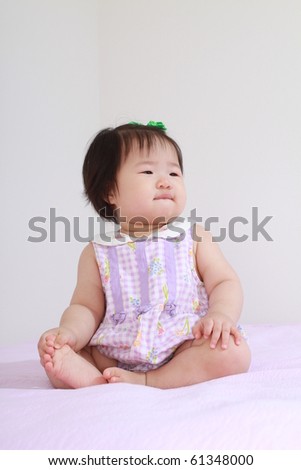 Beautiful ten month old asian baby infant girl in pink and white bodysuit sitting up and looking quizzical