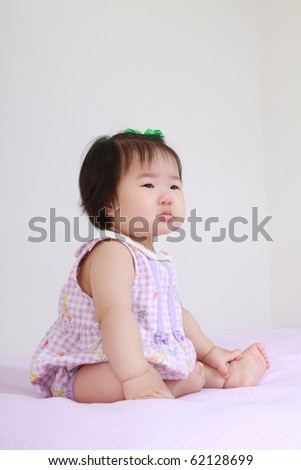 Beautiful Ten Month Old Asian Baby Infant Girl in pink and white bodysuit sitting on bed