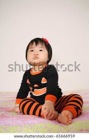 Beautiful eleven month old Asian baby infant Girl dressed up for Halloween and trick or treating in jack o lantern pajamas