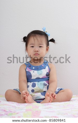 Beautiful Cute Asian Baby Toddler Girl with bows in hair sitting on bed
