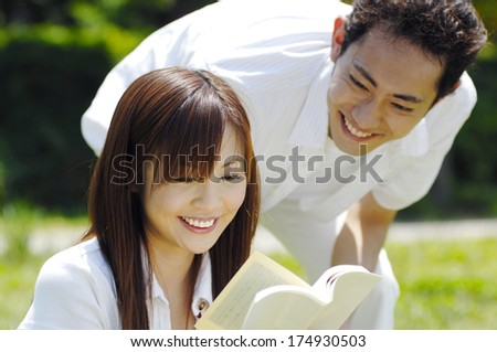 Japanese Man looking at Woman reading a book in the park