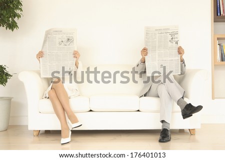 Japanese men and Japanese woman reading the newspaper at both ends of the sofa