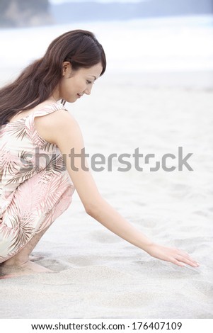 Japanese woman squats down in a sandy beach